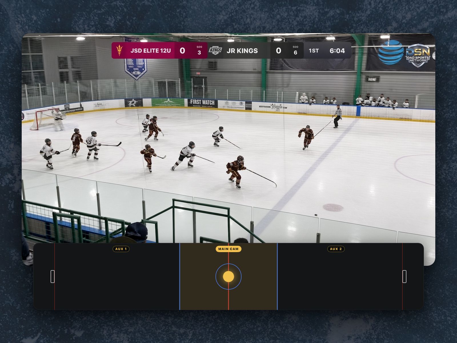 A youth hockey game on air from the main camera at center ice, scoreboard on, above the Touch Track pad: the rink drawn net to net, the stretch between the blue lines lit gold under MAIN CAM with the gold dot on center ice. AUX 1 and AUX 2 cover the two ends.
